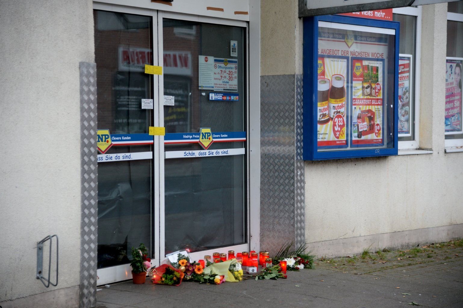 Blumen und Kerzen stehen am 06.12.2014 vor der Tür eines Supermarktes in Hannover (Niedersachsen), wo ein junger Mann am 04.12.2014 bei einem Raubüberfall erschossen worden ist. Hat der Täter auch in Dessau zugeschlagen?