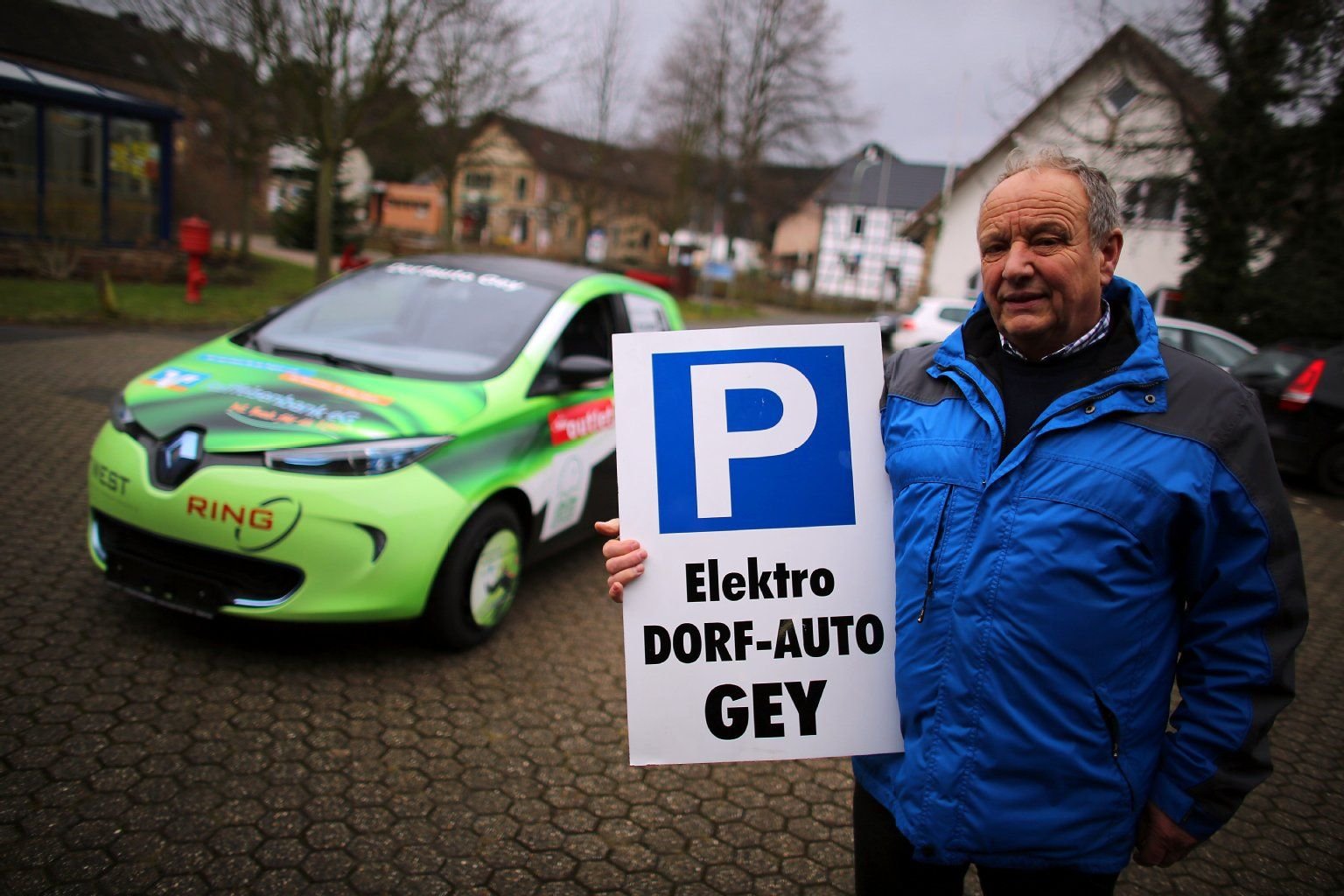 Ortsvorsteher Helmut Rößeler steht in Hürtgenwald (Nordrhein-Westfalen) mit einem Parkschild vor dem Dorfauto.