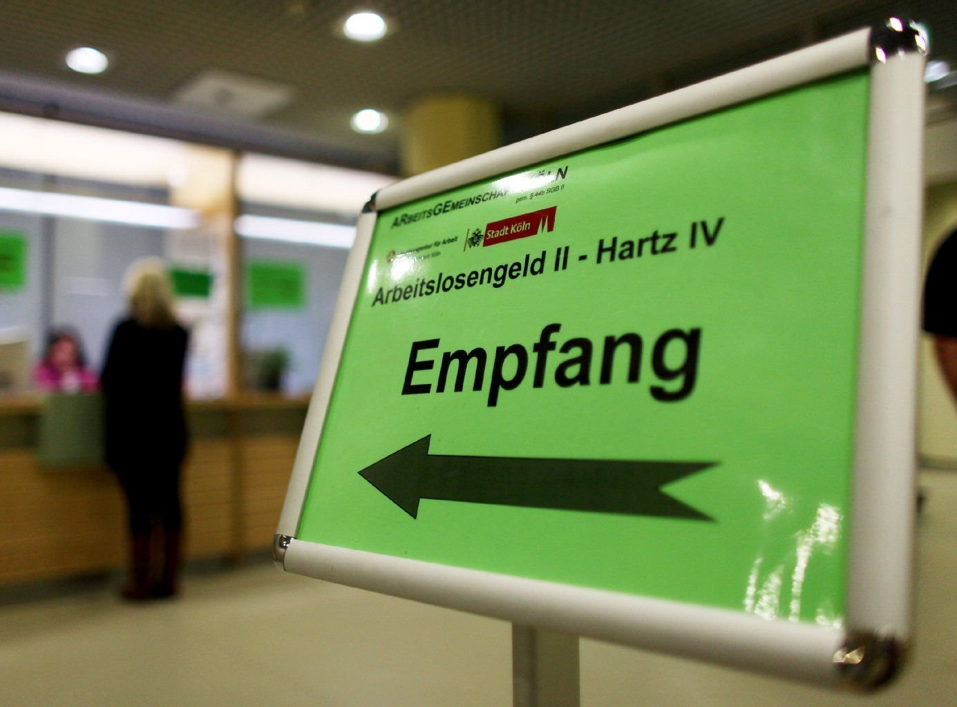 Eine Frau steht in einer Arbeitsagentur am Empfangsschalter, um sich über die Beantragung von Hartz IV bzw. Arbeitslosengeld zu informieren.
