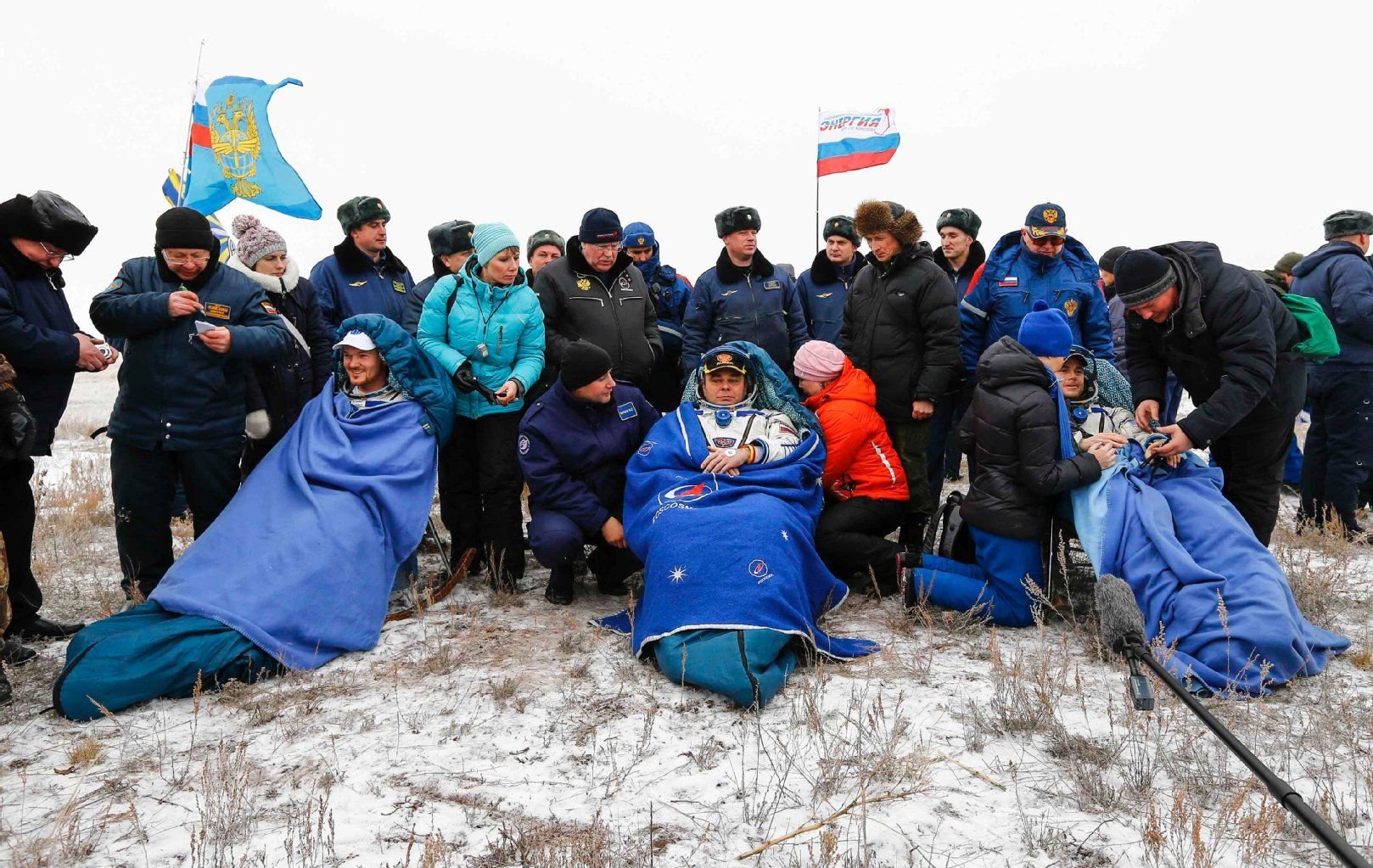 Die Astronauten Alexander Gerst (von links nach rechts), Maxim Surayev aus Russland und Reid Wiseman aus den USA sitzen in Decken gehüllt auf Klappstühlen.