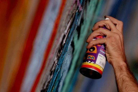 Ein Mann sprüht mit einer aus der Spraydose ein Graffiti.