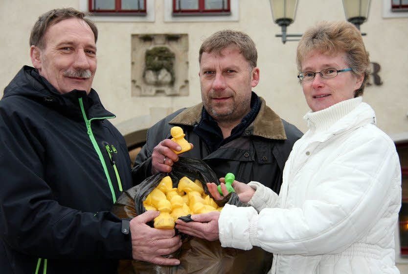 Auf dem Herzberger Markt übergibt Frank Zinnow, Chef des ortsansässigen Gewerbevereins, einen Sack mit „Renn-Enten“ leihweise an Heike Schulze und Michael Pischel (links) aus Annaburg.