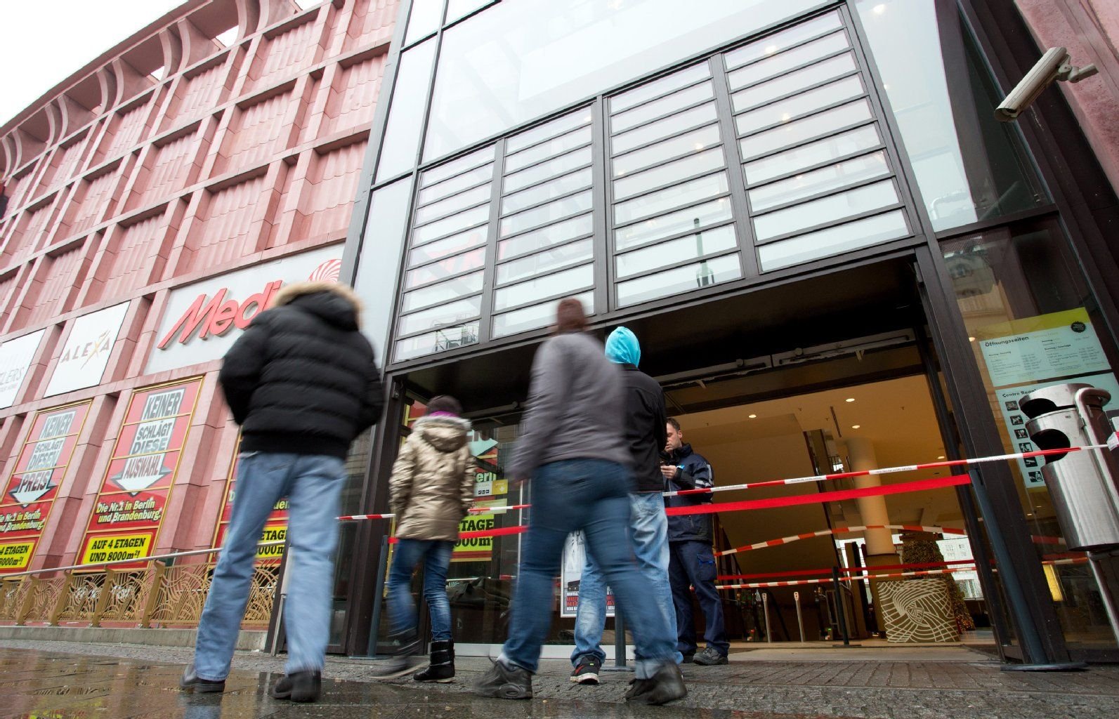 Passanten gehen am zerstörten Eingang des Einkaufszentrums Alexa in der Dircksenstraße in Berlin vorbei. Unbekannte sollen mit einem Kleinwagen in das Einkaufszentrum am Alexanderplatz gerast und in den Mediamarkt eingedrungen sein.