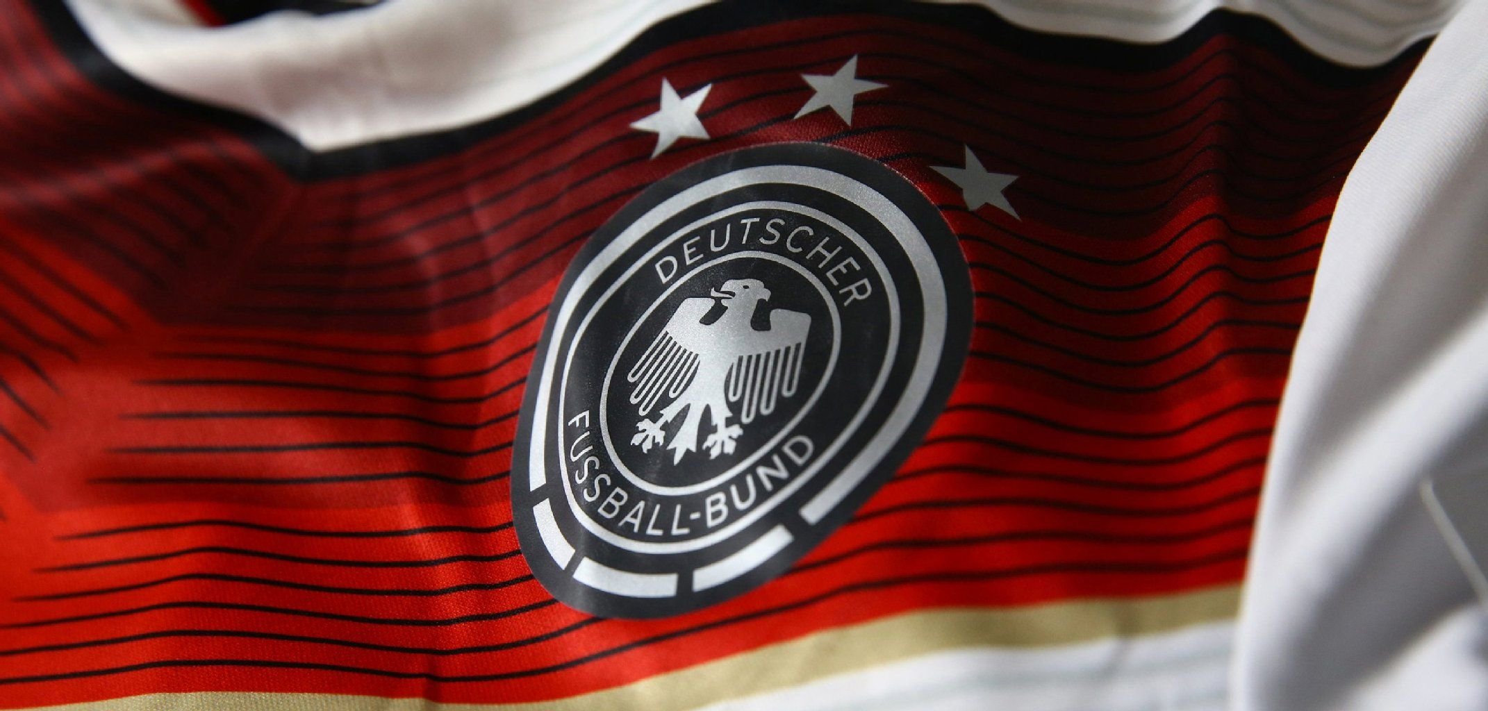Ein breiter roter Streifen ziert das Trikot, umrandet von einem dünnen schwarzen und goldenen Streifen.