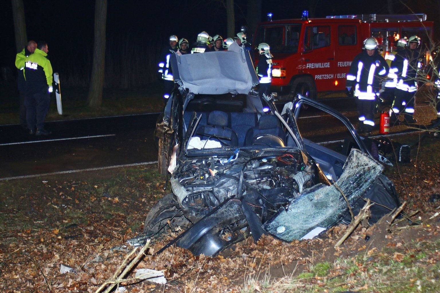 Polizisten und Feuerwehrleute stehen neben dem Wrack des Renault Clio an der Unfallstelle in Bad Schmiedeberg.