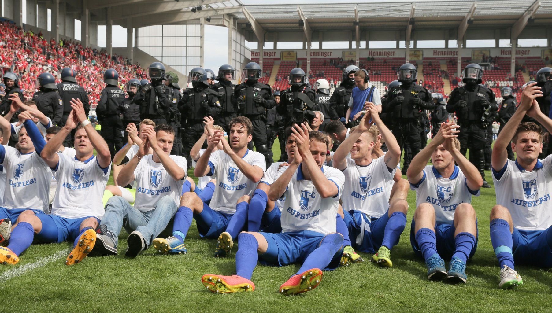 Magdeburger Spieler sitzen jubelnd vor einer Reihe von Polizisten nach dem 3:1-Sieg.