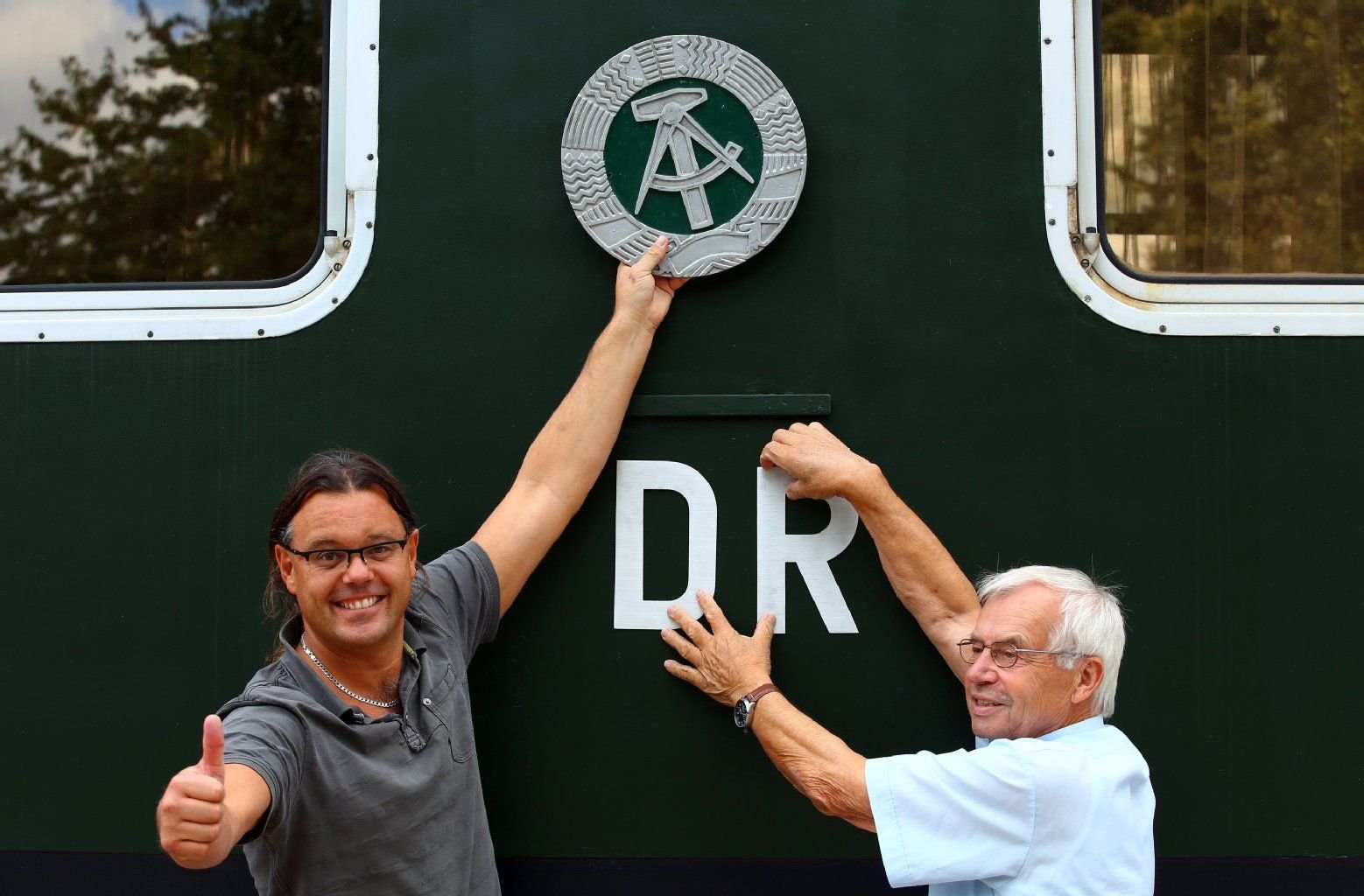Am historischen Salonwagen des ehemaligen DDR-Regierungszuges befestigen Besitzer Holger Hempel (l) und Eisenbahnexperte Peter Falow (r) das DDR-Staatswappen aus Gusseisen sowie die Buchstabenkürzel "DR" für Deutsche Reichsbahn.
