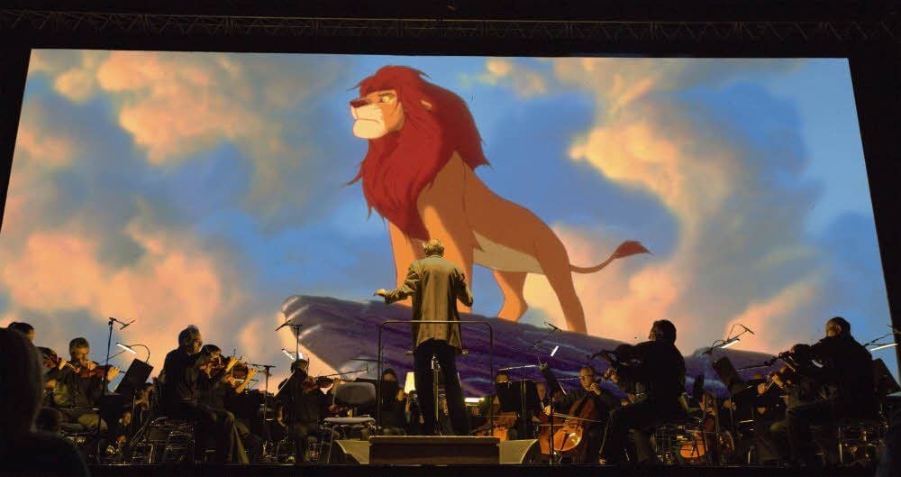 Das Orchester spielt Songs aus „König der Löwen“, während Filmausschnitte auf der Leinwand laufen.