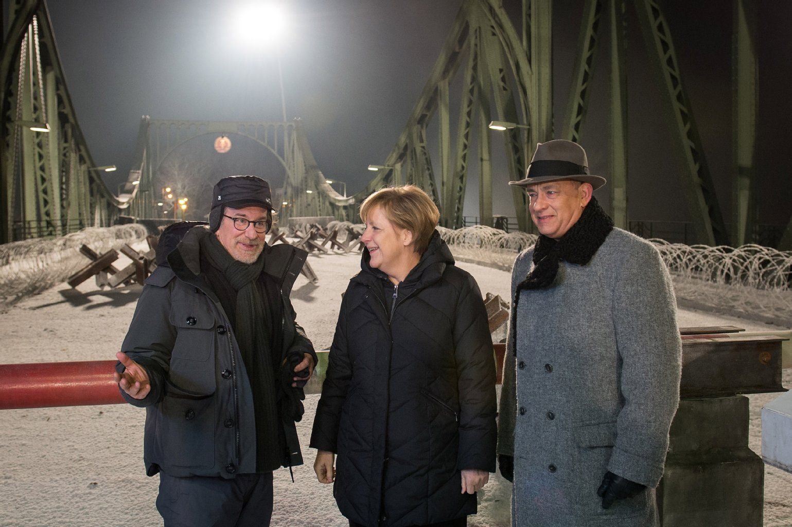 Bundeskanzlerin Angela Merkel (CDU) unterhält sich auf dem Filmset an der Glienicker Brücke in Potsdam (Brandenburg) mit Regisseur Steven Spielberg (l) und Hauptdarsteller Tom Hanks.