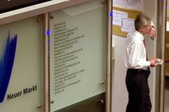 Ein Aktienhändler steht im Handelssaal der Wertpapierbörse in Frankfurt am Main neben einer Tafel mit Namen der am Neuen Markt gehandelten deutschen Firmen. (Archivfoto vom 03.05.2000: dpa)