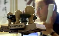Ein Beamter sitzt an einem Schreibtisch, auf dem ein Stempelhalter steht. (Foto: dpa)
