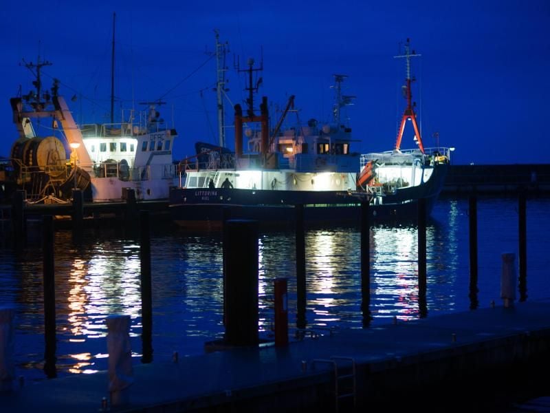 Beleuchtete Fischkutter laufen am Abend zu einer Fangfahrt aus. Foto: Jens Büttner/Archiv