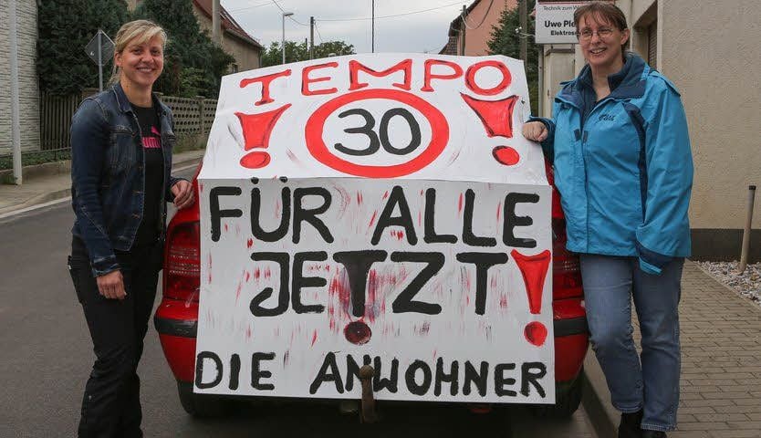 Susen Günther (links) und Ines Thiele vor dem Plakat, das für die Von-Seydlitz-Straße in Reichardtswerben ein Tempolimit fordert.