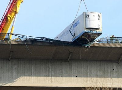 Mit einem Kranwagen versuchen Rettungskräfte einen LKW-Auflieger von der Brohltalbrücke der Autobahn A61 bei Niederzissen zu bergen (FOTO: DPA)