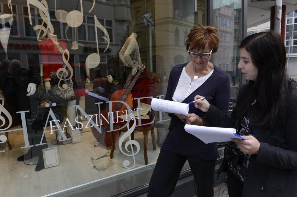 Hier spiegelt sich die Stadt sinnfällig in einem Händel-Schaufenster. Gabriele Kirsten und Julia Gantschew, Jurorinnen beim Schaufenster-Wettbewerb zu den Händelfestspielen, begutachten die Präsentation des Kaufhauses Fischer in der „Rolltreppe“.