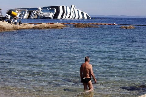 Ein Tourist geht ins Meer, während im Hintergrund das Wrack der Costa Concordia zu sehen ist. (FOTO: DPA)