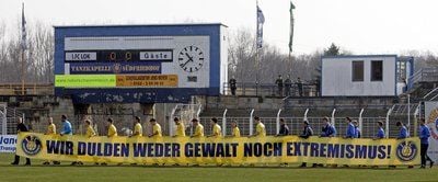 Mit einem Spruchband mit der Aufschrift "Wir dulden weder Gewalt noch Extremismus" laufen die Spieler des 1. FC Lok Leipzig Bruno-Plache-Stadion in Leipzig ein (Archivbild von 2008).