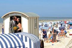 Ein Hochzeitspaar steht auf der Nordseeinsel Norderney nach der standesamtlichen Trauung mit der Standesbeamtin Bettina Mai (l.) in einem Badekarren, in dem das Standesamt untergebracht ist. (Foto: ddp)
