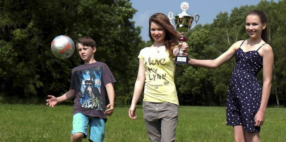Kevin Güttler lässt schon mal den Ball tanzen. Maria Rauh und Klara Niehaus präsentieren den Pokal, um den es geht.