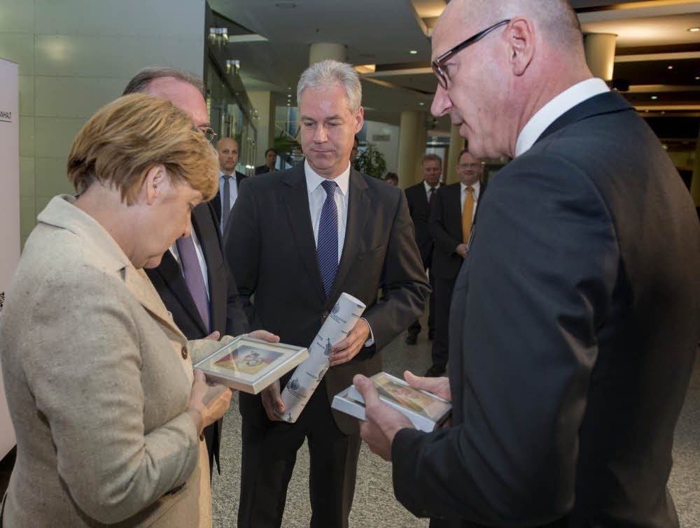 Kanzlerin Angela Merkel erhält von Tilo Schelsky (rechts), Geschäftsführer der Mediengruppe Mitteldeutsche Zeitung, und MZ-Chefredakteur Hartmut Augustin die Sondermarke „25 Jahre Deutsche Einheit“ des MZZ-Briefdienstes.