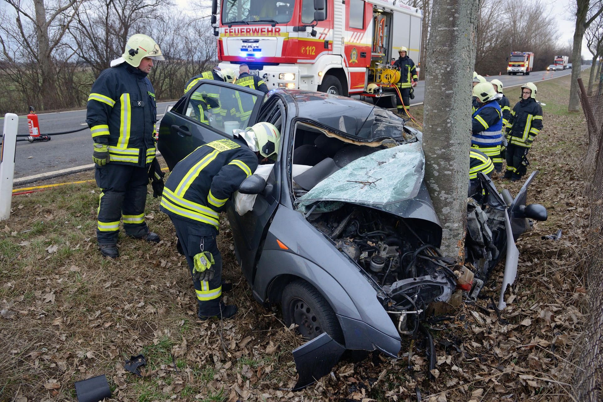 Feuerwehrleute stehen auf der B79 zwischen Quedlinburg und Münchenhof neben dem total zerstörten Auto.