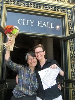 Die Kanzleiangestellte Meli Kigasari und die Anwältin Elisabeth Kristen (r) schwenken einen Blumenstrauß und ihre frisch beantragten Heiratspapiere in San Francisco. Mit einer knappen Stimmenmehrheit erklärte der Supreme Court des US-Westküstenstaates das bisherige Verbot der Homo-Ehe für verfassungswidrig. (Foto: dpa)