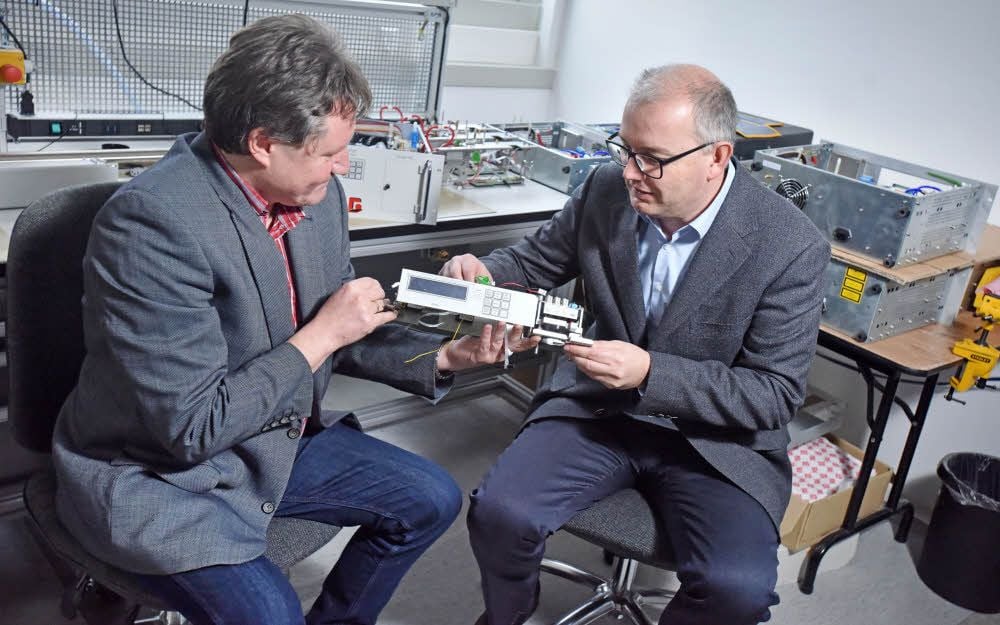 Geschäftsführer Marco Signori (re.) und Produktionsleiter Torsten Straßburger nehmen im neuen Forschungs- und Entwicklungslabor ein Teil eines Umweltstaubmessinstrumentes unter die Lupe.