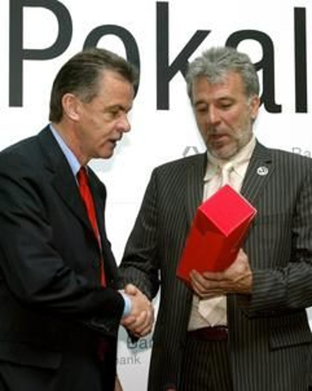 Unter der Aufschrift " Pokal" geben sich Ottmar Hitzfeld (l), der Trainer des Fußball-Bundesligisten FC Bayern München, und Eric Gerets, Trainer des 1. FC Kaiserslautern, am Montag (19.05.2003) in Berlin die Hand. Gerets überreicht gleichzeitig eine Flasche Rotwein zum Gewinn der Deutschen Meisterschaft. Auf einer Pressekonferenz nahmen die beiden Trainer zum am 31.05.2003 in der Hauptstadt statt findenden Pokalendspiel zwischen den beiden Mannschaften Stellung. (Foto: dpa)