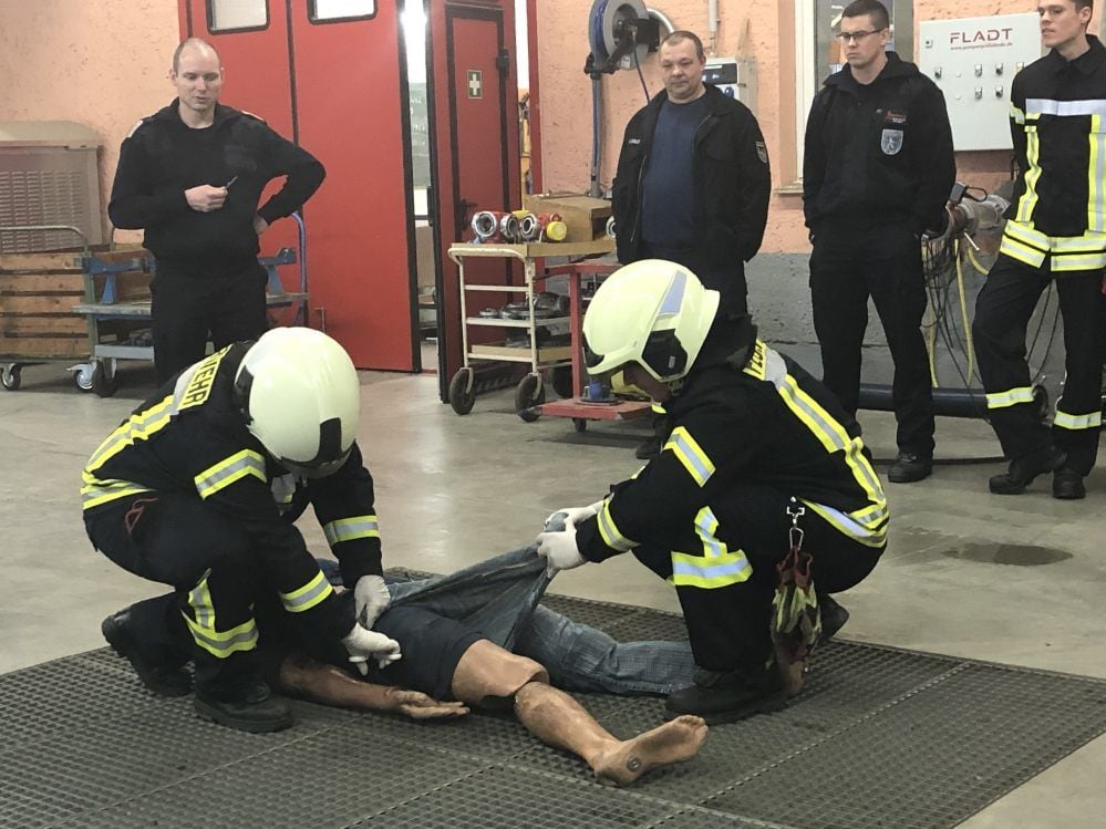 Notdekontamination bei einer Person wird geübt: Zwei Einsatzkräfte entfernen gemeinsam die mit einem Gefahrstoff belastete Kleidung.
