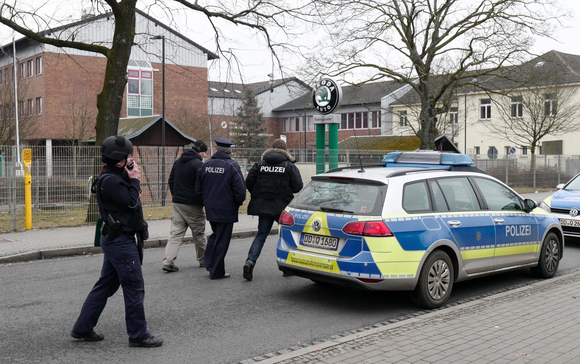 Polizisten stehen in Borsdorf vor einer Berufsschule neben ihren Fahrzeugen.
