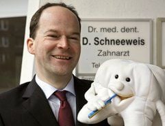 Der Zahnarzt Dr. Detlev Schneeweis steht vor seinem Praxisschild in Hamburg. (Foto: dpa)