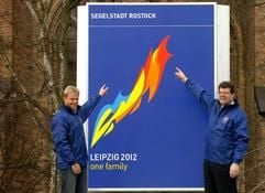 Der Oberbürgermeister der Hansestadt Rostock, Arno Pöker (r) und der Vorsitzende des privaten Fördervereins Rostock-Olymp, Hansjörg Kunze, präsentieren am Donnerstag (04.03.2004) in Rostock das neue Logo für die Bewerbung Rostocks um die Ausrichtung der olympischen Segelwettbewerbe 2012. Das neue Symbol steht auf dem Informationspavillon am Neuen Markt der Hansestadt. (Foto: Jens Büttner, dpa)