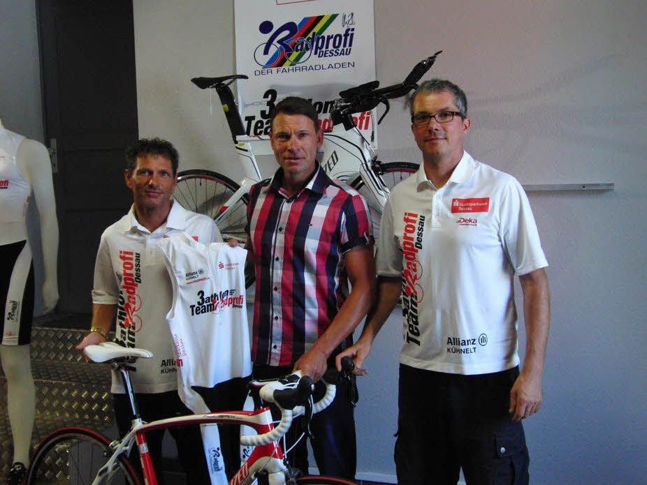 Trainer Harry Kühnelt (li). übergibt zusammen mit Teamchef Thomas Siegel (r.) dem neu zum Team stoßenden Renzo Wernicke seinen Triathlonanzug. Am Sonntag soll mit seiner Hilfe Platz zwei gesichert werden.