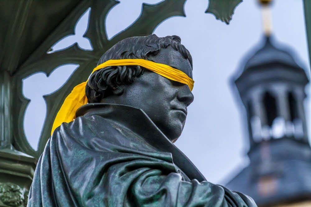 Die Augenbinde (kleines Foto) war am Montag schnell wieder weg vom Luther-Denkmal in Wittenberg. Am Dienstag folgten die Blumen: Martin Luther wurde am 10. November 1483 in Eisleben geboren.