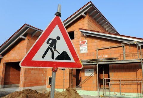 Ein Baustellenschild steht vor dem Rohbau eines Einfamilienhauses.