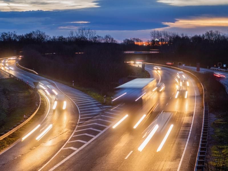 Fahrzeuge fahren in der Morgendämmerung über eine Bundesstraße und Autobahn. Foto: Julian Stratenschulte/dpa