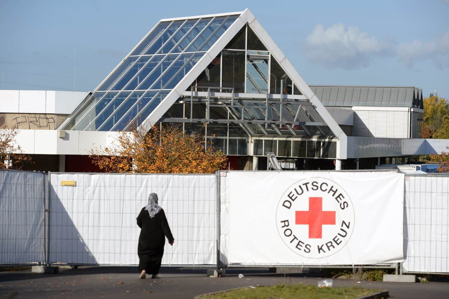 Ein Frau geht am 23.10.2015 in Niederau (Sachsen) vor einer Unterkunft für Flüchtlinge an einem Logo des Deutschen Roten Kreuzes vorbei.