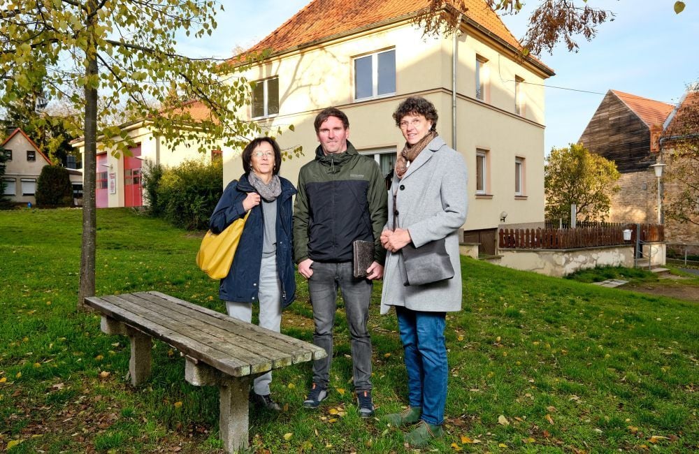 In Teicha wird derzeit ein neuer Arzt gesucht. Er soll in das Haus Dorfplatz 10a (Hintergrund) ziehen. Andrea Uhlenhaut, Ortsbürgermeister Steffen Schulze und Marion Winkler (v.l.n.r.) werben für den Standort.