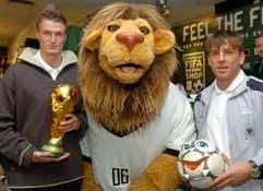 Die Fußball-Nationalspieler Bernd Schneider (Bayer Leverkusen, r) und Robert Huth (FC Chelsea London) stehen am Montag (15.11.2004) in Leipzig bei der Eröffnung eines offiziellen «FIFA WM 2006 TM Shop» mit dem sprechenden Fußball «Pille» und dem Original FIFA WM-Pokal neben dem WM-Maskottchen «Goleo VI». (Foto: dpa)