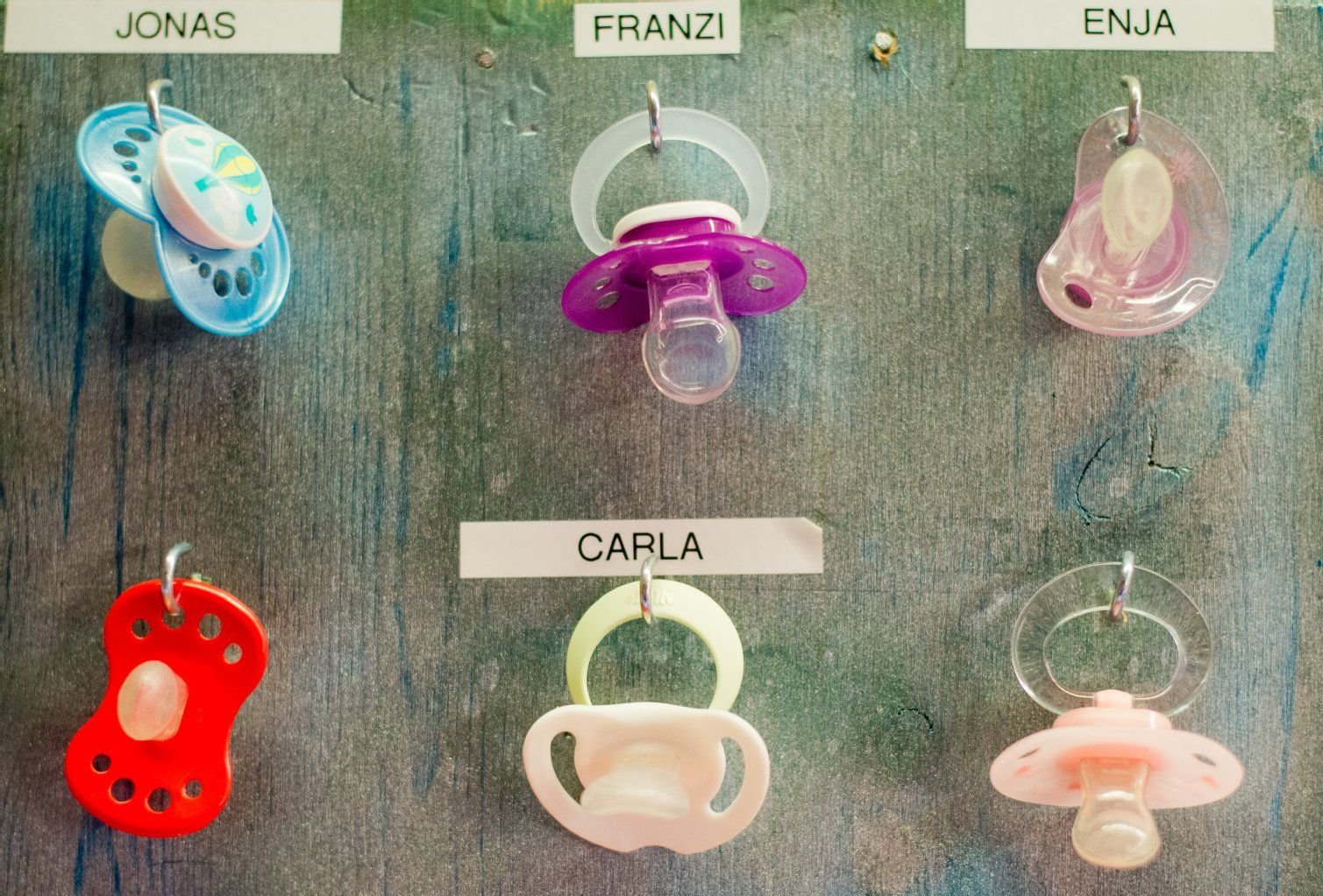 Schnuller von Kleinkindern hängen an einem Brett in einer Kindertagesstätte