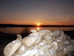 Ein romantischer Sonnenuntergang ist am Sonntag (05.01.2003) hinter überfluteten Wiesen an der Unstrut nahe dem thüringischen Ort Artern zu sehen. Auf den Sandsäcken, die hier zur Eindämmung des Hochwassers gestapelt sind, liegt nach dem Regen der vergangenen Tage nun der ersehnte Schnee. Der Frost brachte am Sonntag nach Angaben des Krisenstabes im Kyffhäuserkreis leichte Entspannung, weil die Dämme fester wurden. Ein Deich an einem Flutkanal zwischen Reinsdorf und Artern war am Samstagabend (04.01.2003) auf einer Länge von drei Metern gesprengt worden. Rund 250 Hektar unbewohntes Gebiet wurden damit geflutet. (Foto: dpa)