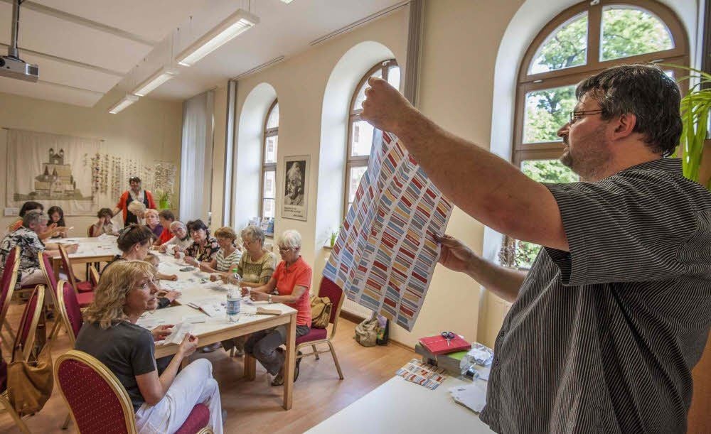 Maik Ulbricht erklärt den Kursteilnehmerinnen, wie ein Papierkranich gefaltet wird.