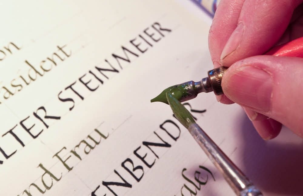 Hannelore Heise bestreicht mit einem Pinsel ihre Brausefeder, mit der sie den Text im Goldenen Buch schreibt.