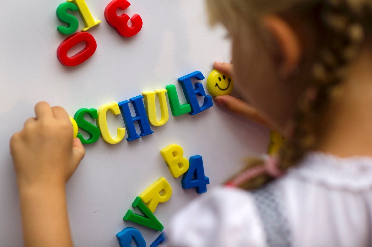 Ein Kind schreibt mit Magnetbuchstaben das Wort "Schule" an eine Magnettafel.