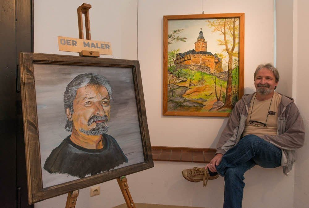 Reiner Wiedenbeck neben seinem Selbstporträt und einer Ansicht der Burg Falkenstein.
