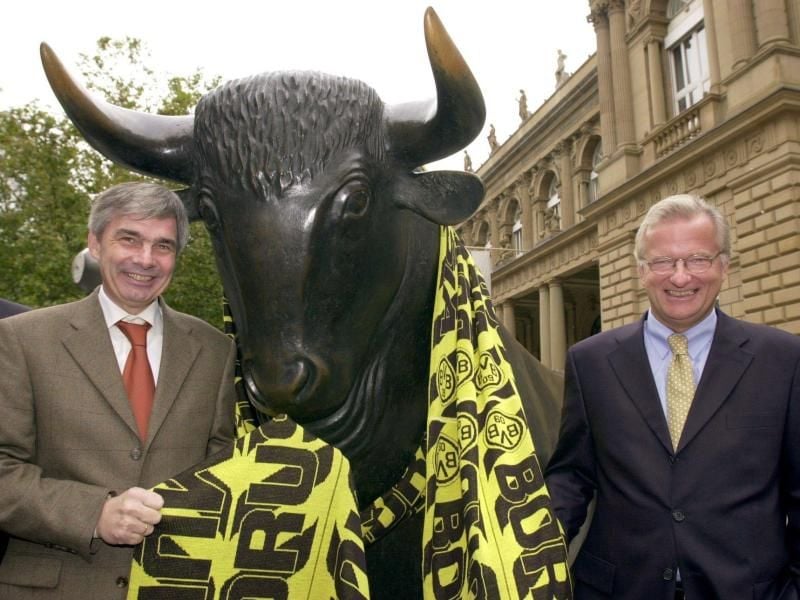 Gerd Niebaum (r), damaliger BVB-Präsident, und der damalige BVB-Manager Michael Meier stehen am 31.10.2000 vor der Frankfurter Börse mit einem übergroßen Fanschal am Bronzebullen. Foto: Arne Dedert/dpa/Archivbild