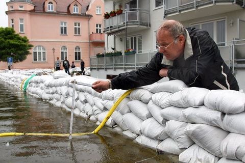 Ein Mann prüft am Freitag in einer überfluteten Straße im Stadtteil Fürstenberg in Eisenhüttenstadt (Kreis Oder-Spree) in Brandenburg an der Oder mit seinem Zollstock den Pegel. (FOTO: DPA)