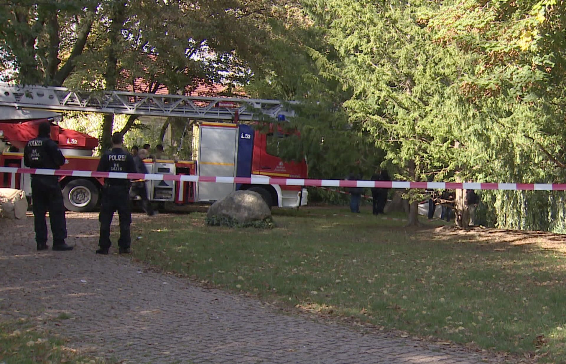 Einsatzkräfte der Polizei und Feuerwehr stehen am Ufer des Dorfteichs in Berlin-Lichtenrade.