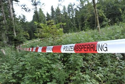 Ein Absperrband der Polizei hängt in einem Waldstück am Ortsausgang von Tacherting im Landkreis Traunstein (Oberbayern), wo am frühen Morgen die blutüberströmten Leichen zweier 37- und 44-jährigen Männer gefunden worden waren. (FOTO: DPA)