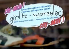 Ein zweisprachiger Aufkleber der Aktion «grenzenlos schöner einkaufen» hängt Anfang März 2004 im ostsächsischen Görlitz an der Eingangstür eines Schuhladens. Die Einzelhändler der deutsch-polnischen Grenzstadt sind auch auf die Käufer aus Zgorzelec von der anderen Seite der Neiße angewiesen. Knapp zwei Monate vor dem EU-Beitritt Polens und Tschechiens machen im sächsischen Grenzgebiet viele Händler gute Geschäfte mit Kunden aus den Nachbarländern. Zurzeit gibt es noch den Anreiz, bei einem Einkaufsbummel im jeweiligen Nachbarland anschließend die Mehrwertsteuer zurück zu erhalten. Mit dem 1. Mai entfällt diese Regelung. (Foto: dpa)
